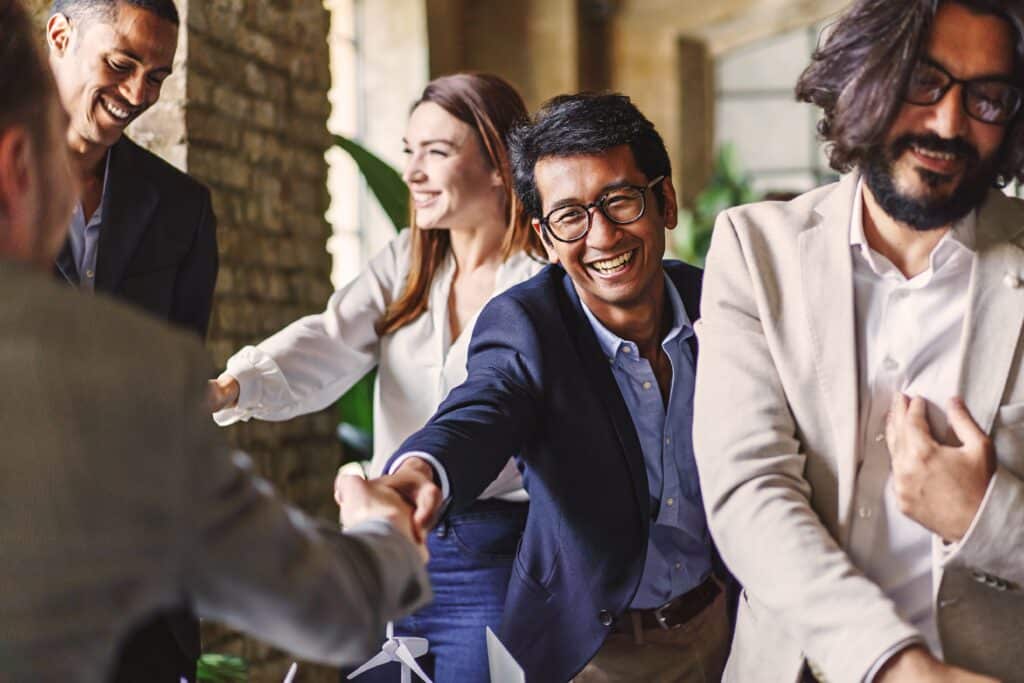 Four people in business attire are smiling and shaking hands in a brightly lit office setting, celebrating innovation for financial services.